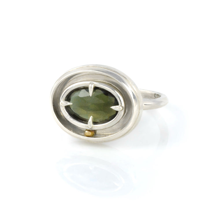 A kinetic solitaire ring by Emma Brooke featuring a green gemstone. The ring is silver, with a yellow gold rolling ball, on a white background.