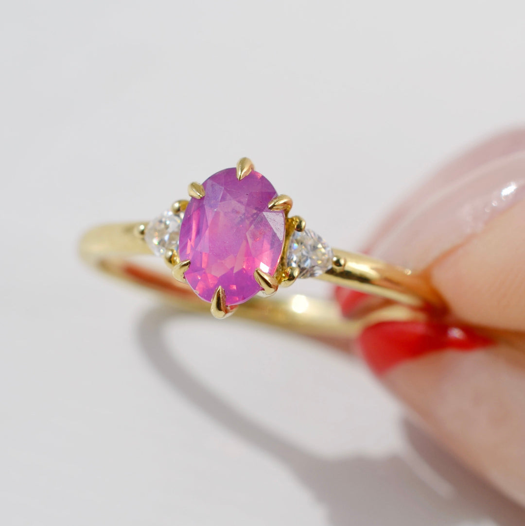 Gold ring with a pink gemstone held by a hand on a light gray background