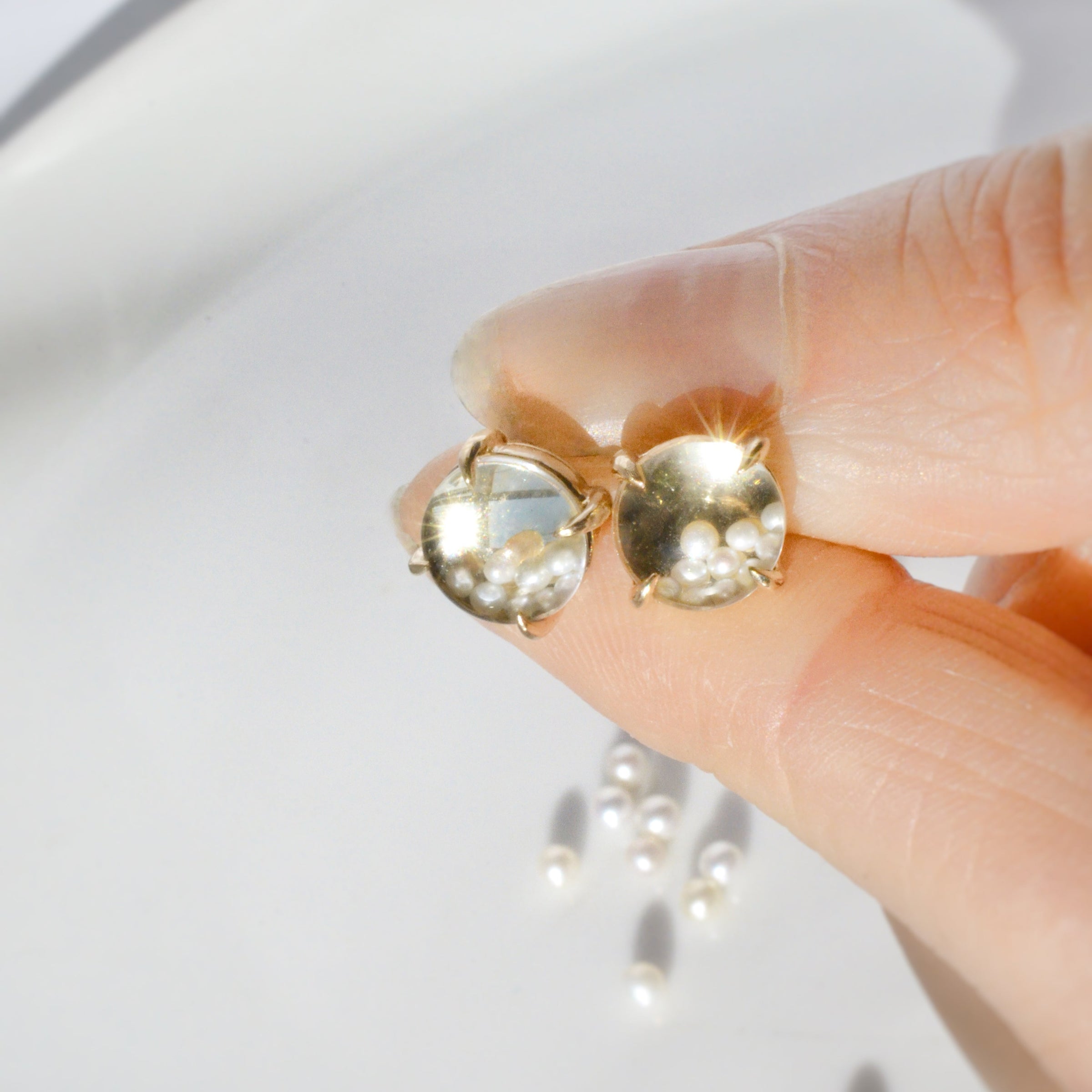 Gold earrings with kinetic pearls held by a hand against a white background