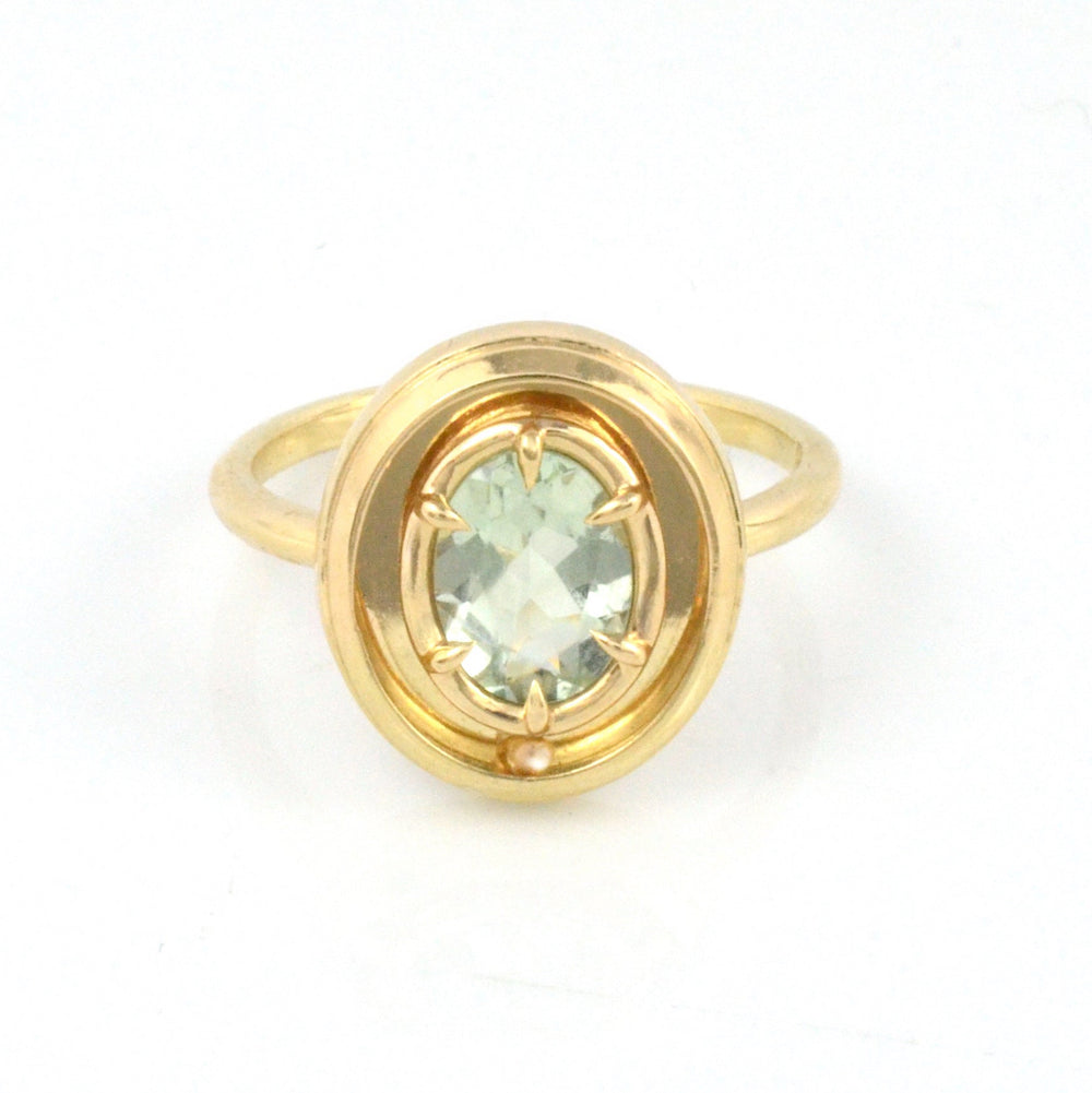 Gold ring with a green gemstone on a white background, featuring a moving gold ball.