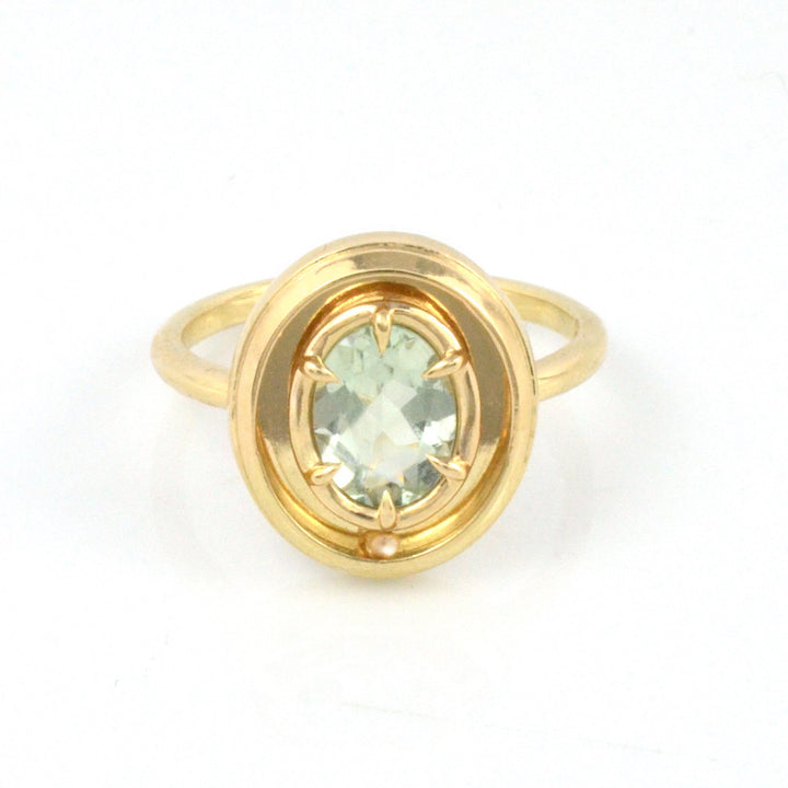 Gold ring with a green gemstone on a white background, featuring a moving gold ball.