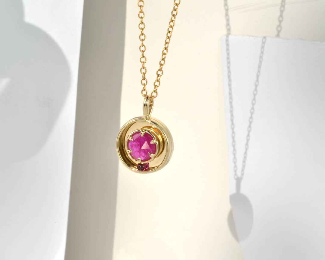 Gold necklace with a pink ruby gemstone on a white background