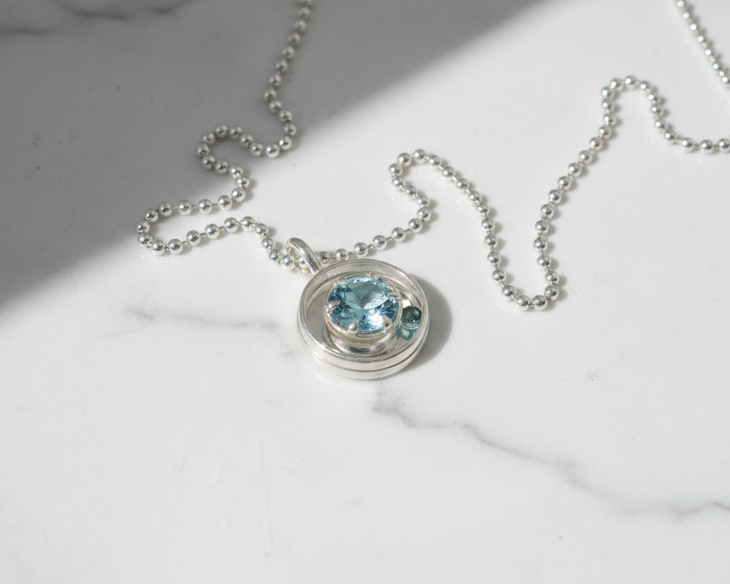 Silver necklace with a blue gemstone pendant on a marble surface