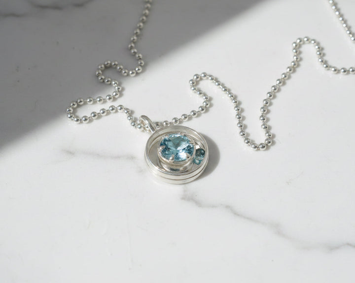 Silver necklace with a blue gemstone pendant on a marble surface