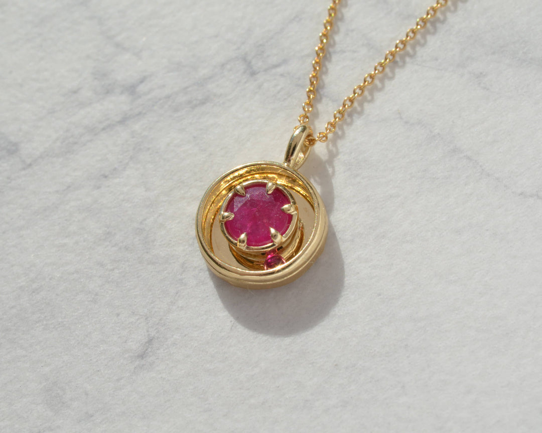 Gold necklace with a red gemstone pendant on a marble background