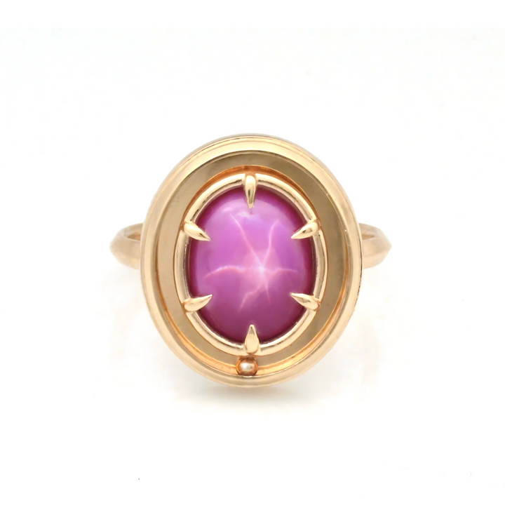 A large star ruby solitaire with a kinetic rolling piece, in a luxury 14K anxiety ring by Emma Brooke. The ring is yellow gold, with a large, oval, hot-pink ruby.