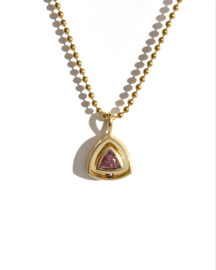 a gold pendant with a burgundy pink garnet in a trillion cut. the necklace has a moving rolling garnet ball.