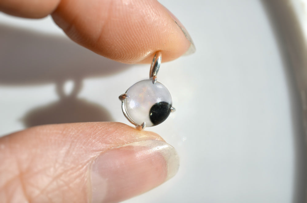 Close-up of a hand holding a small googly-eye shaped pendant with a rolling black stone.