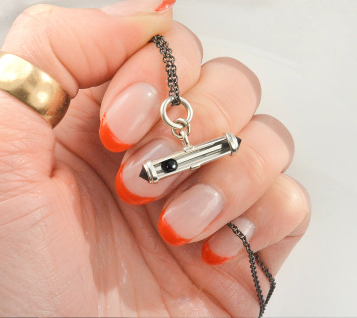 Hand holding a necklace with a silver an onyx kinetic pendant featuring a rolling black gemstone sphere.