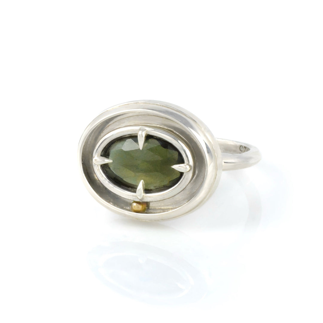 A kinetic solitaire ring by Emma Brooke featuring a green gemstone. The ring is silver, with a yellow gold rolling ball, on a white background.