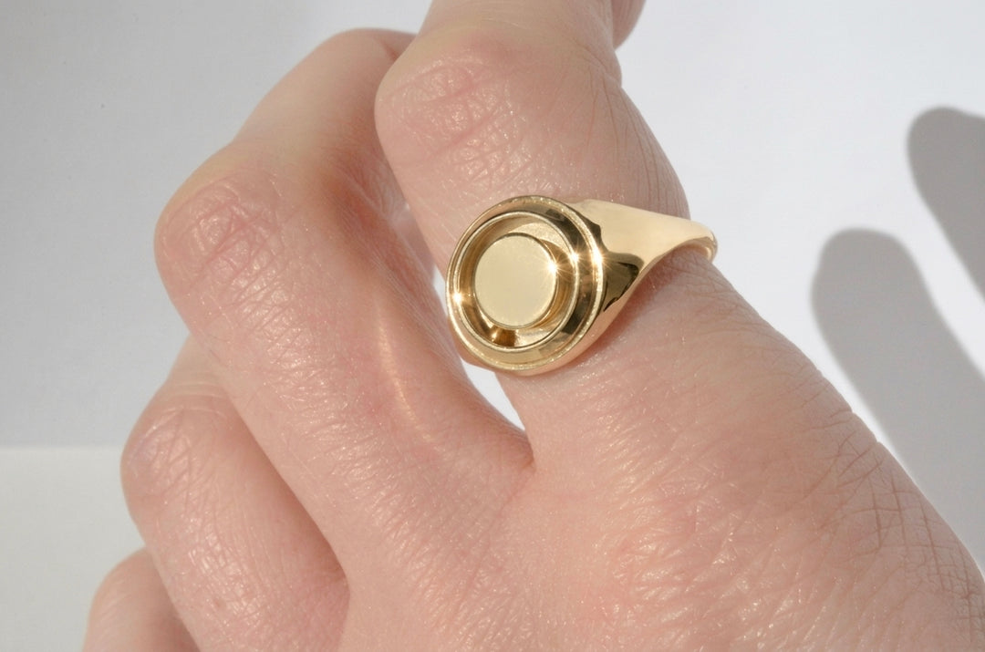 Gold kinetic signet ring featuring a rolling gold ball. Modeled on a hand against a neutral background.
