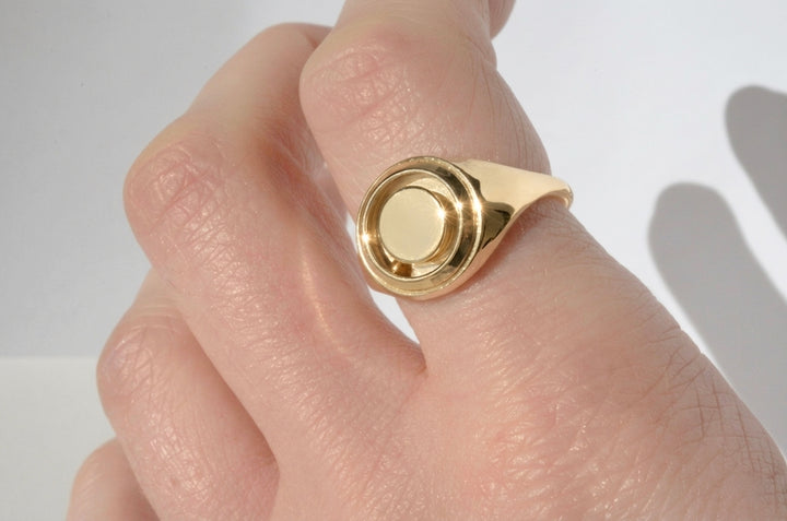 Gold kinetic signet ring featuring a rolling gold ball. Modeled on a hand against a neutral background.