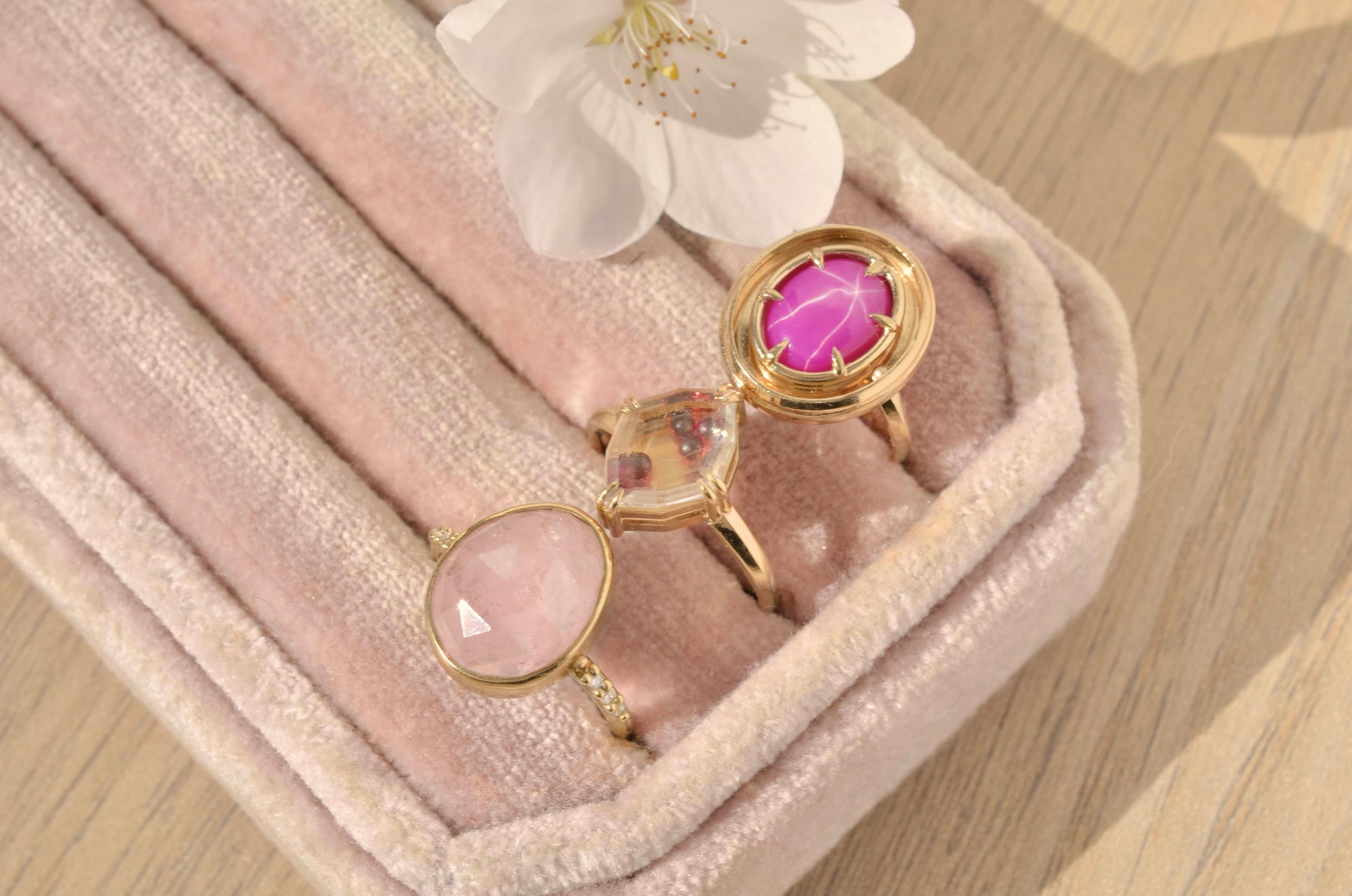 3 rings with pink gemstones on a velvet tray, shown in the sunlight with a cherry blossom.