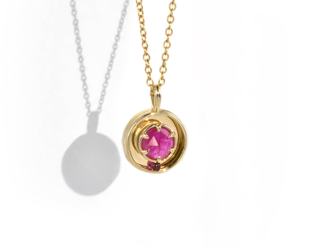 A large pink ruby set in a yellow gold necklace, with a kinetic ruby ball.