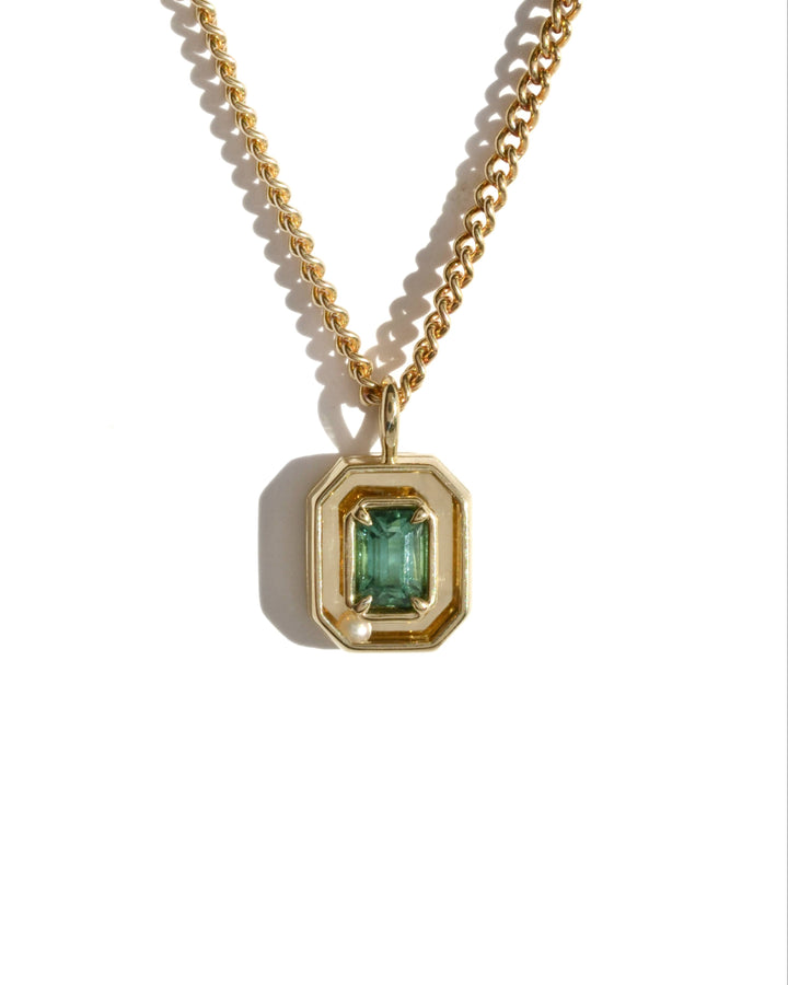 a gold pendant with a teal green tourmaline in an emerald cut. the pendant features a kinetic, rolling white pearl.