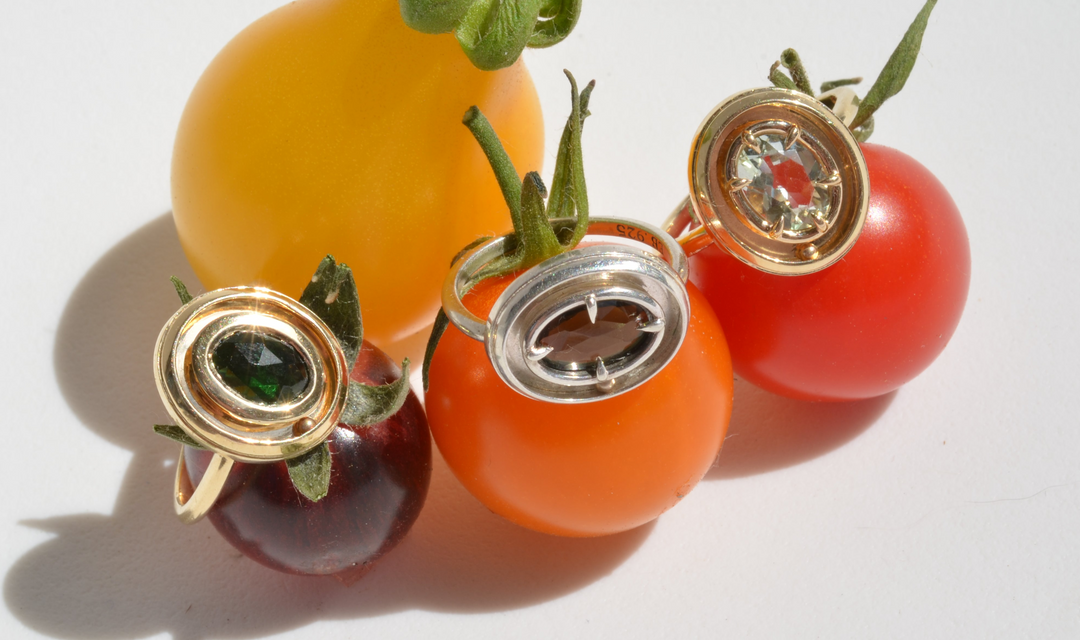 rings with green gemstones perched on top of colorful cherry tomatoes