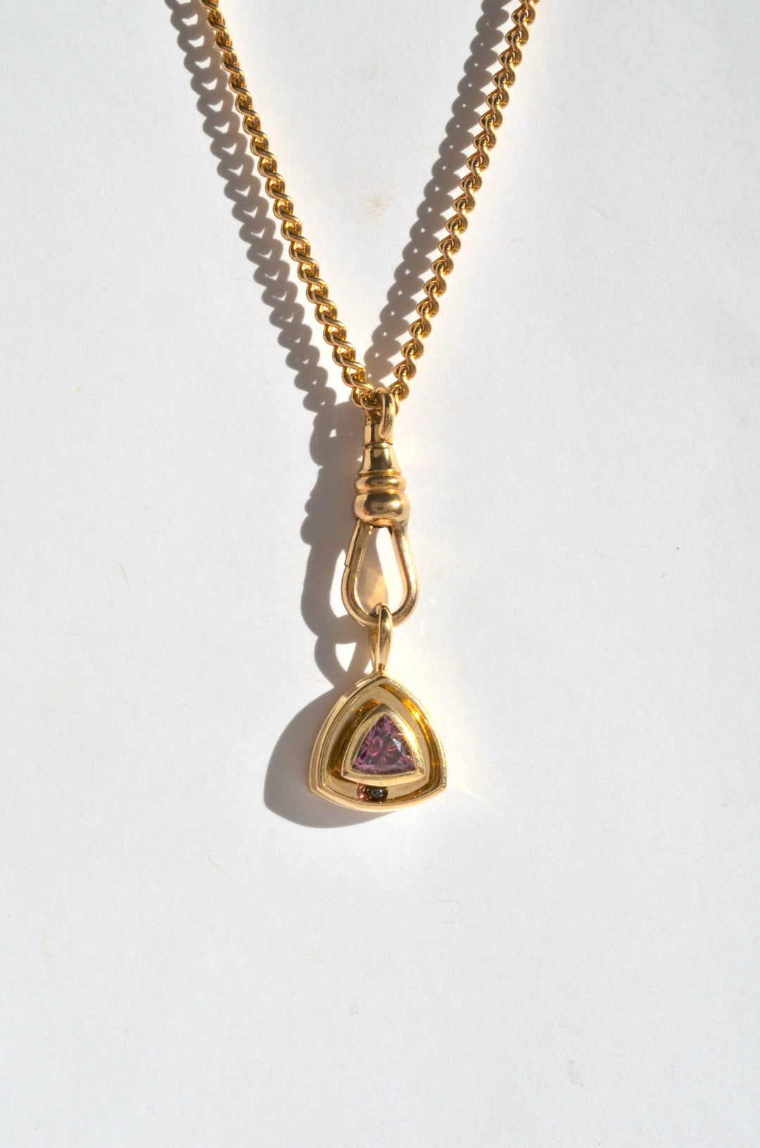 a gold and garnet triangular charm on a curb chain with a dog clip charm clasp