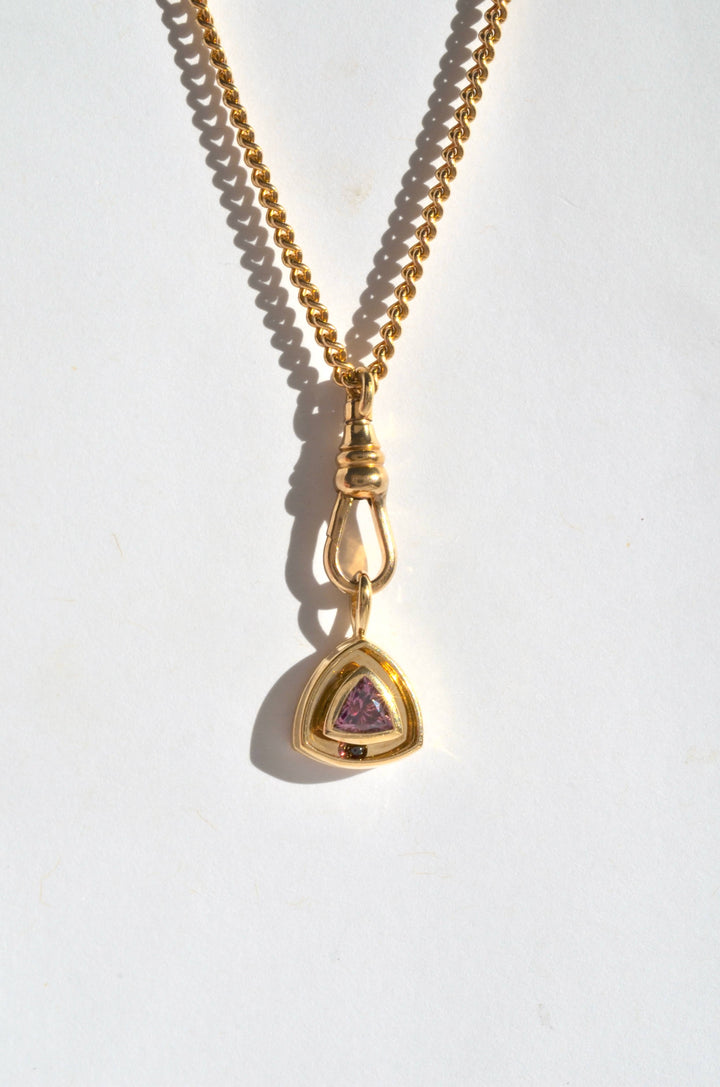 a gold and garnet triangular charm on a curb chain with a dog clip charm clasp
