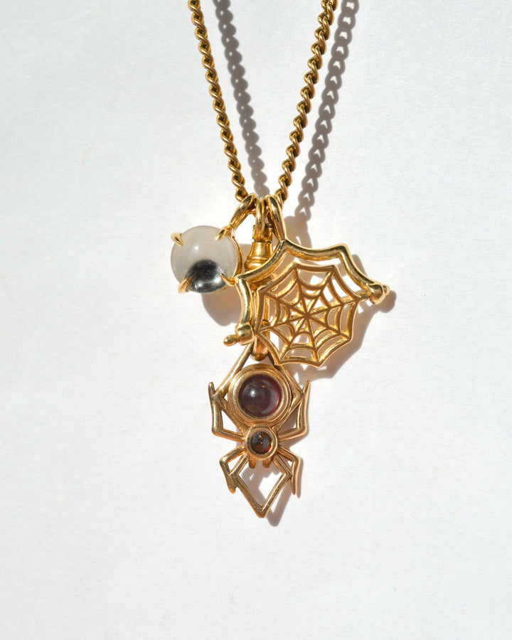 A gold-toned charm necklace featuring a spider, a spider web, and a googly eye charm, shown on a plain white background. the charms are all kinetic and can move.