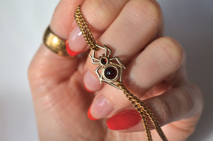 A close-up of a hand holding a gold chain necklace with a spider-shaped charm, showing how the charm can be used as a connector to link 2 chains.