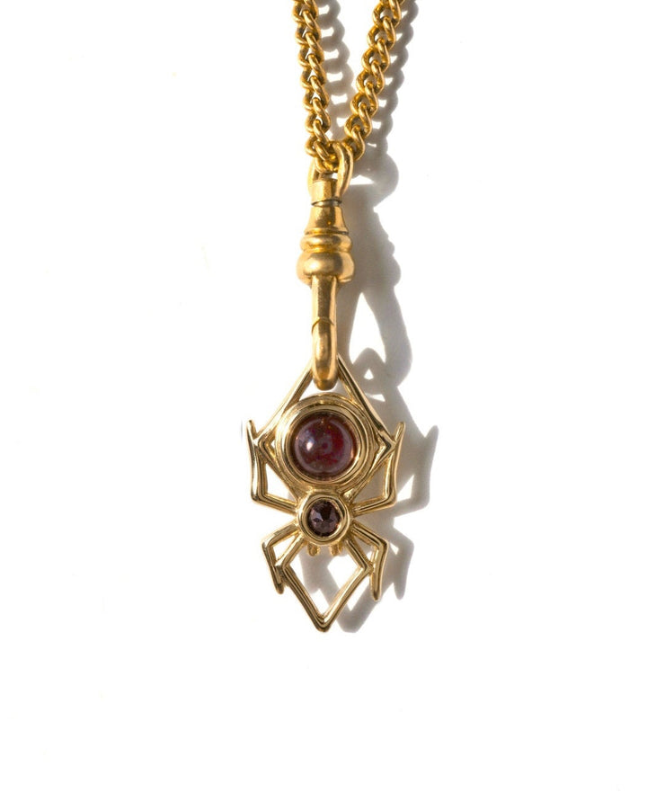 A gold spider pendant necklace featuring a dark red gemstone sphere that can roll in place, suspended from a vintage gold chain on a white background.