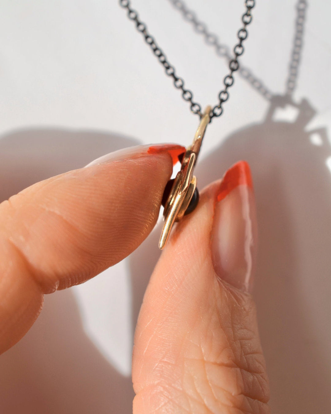 A close-up side view of a hand holding the spider orb pendant, showing how the garnet sphere can be rolled between your fingers.